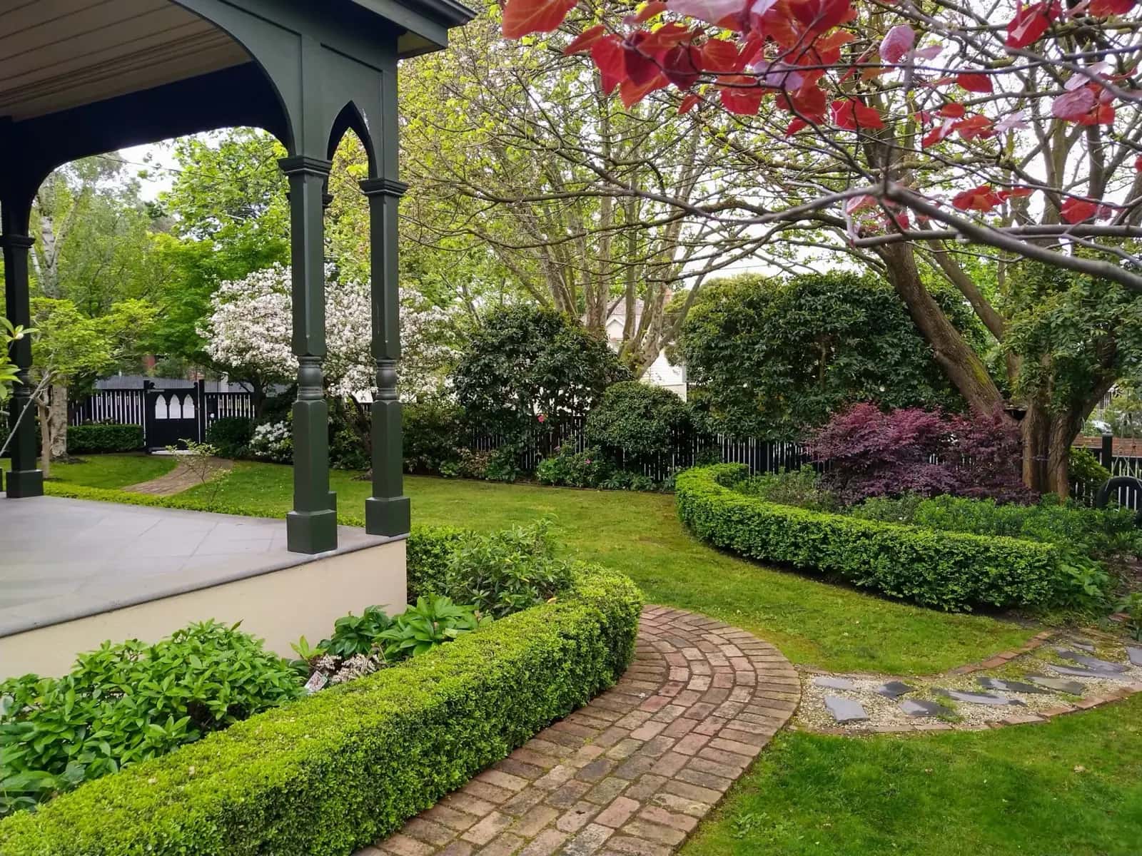 Manicured Victorian garden with curved brick pathway, box hedging, flowering dogwood, and red Japanese maple maintained by ABS Horticulture
